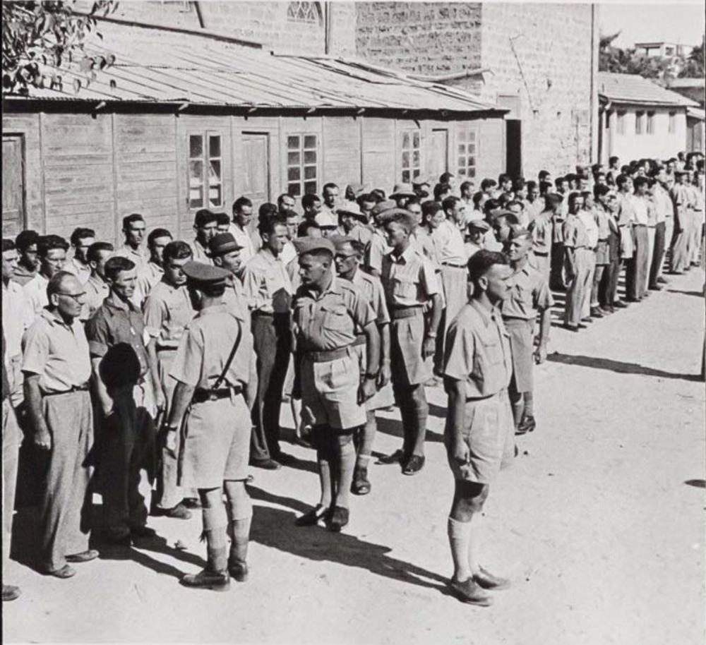 The photo shows a line of Jewish soldiers in formation as Ernest Frank Benjamin, a Jewish Canadian brigadier, inspects the new recruits. A seasoned officer, Benjamin was deeply committed to the Brigade and even learned Hebrew in preparation for his command.